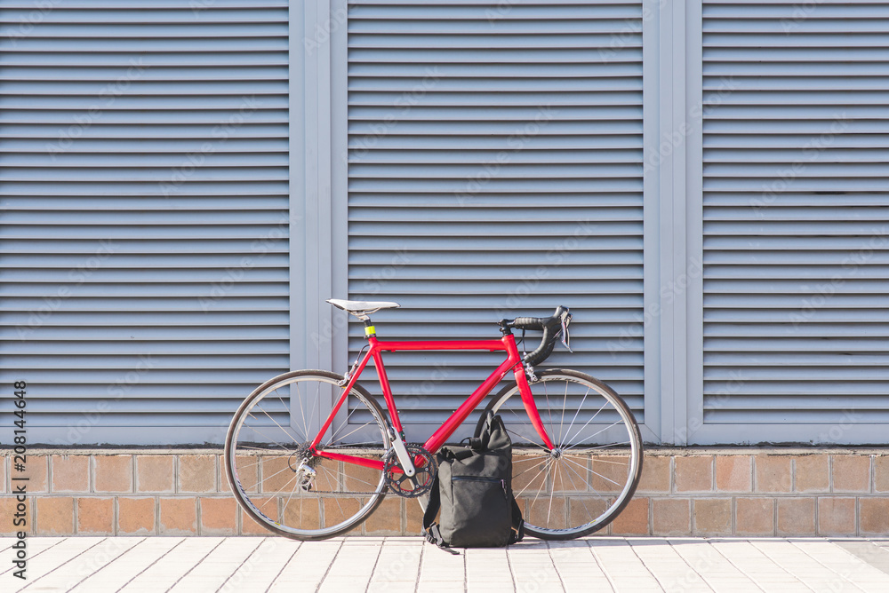 Red road bike and backpack against a gray wall background. Sports concept.Copyspace.