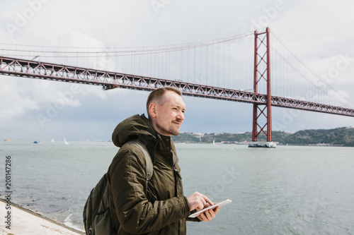 A person uses a tablet to communicate with friends or looks at a map, or calls a taxi, or something else. Bridge April 25 in Lisbon in Portugal in the background