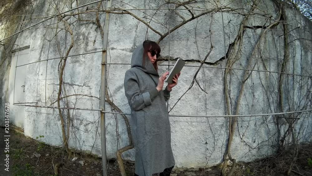 pretty brunette in a gray cardigan using digital tablet at the park in front of the concrete wall with dry vine 3 pretty brunette in a gray cardigan using digital tablet at the park in front of the concrete wall with dry vine 3