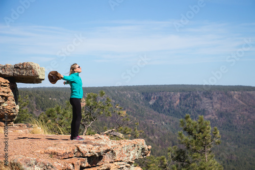 young woman open her arms, holding her hat and feel free at the edge