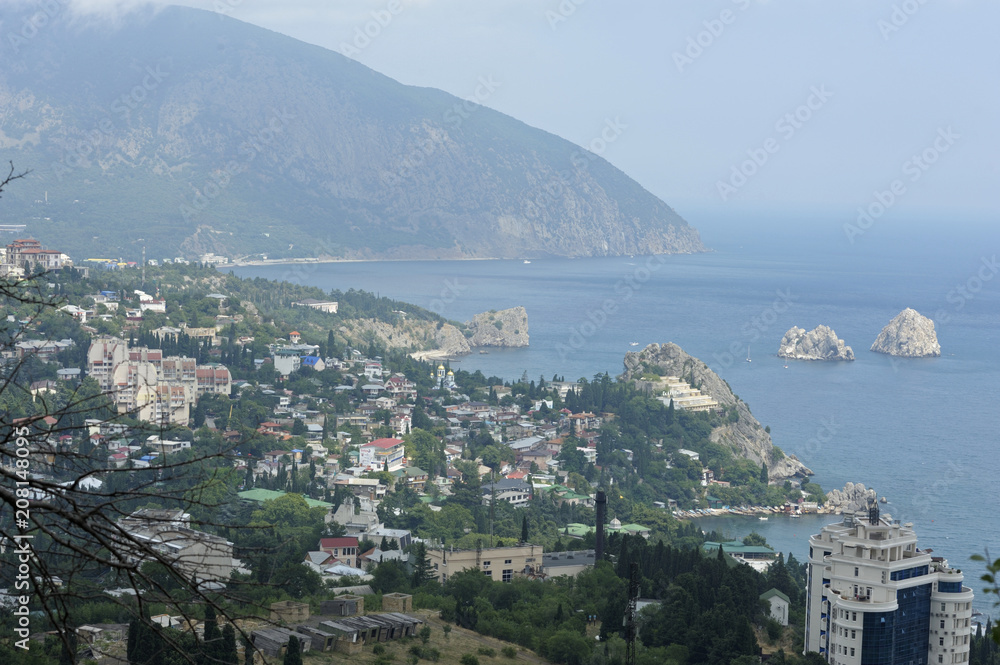 View of the resort town Gurzuf: sea front, beach, buildings and mountains in the fog. June 10, 2017. Gursuf, Crimea