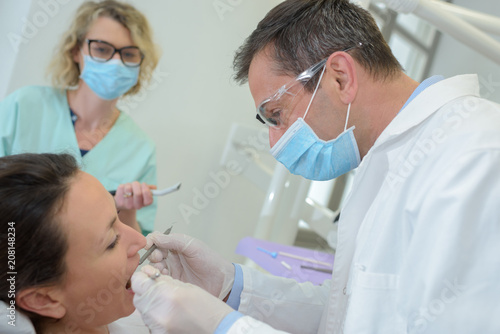 dentist with assistant examining womans teeth in the dentists chair