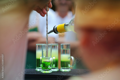 bartender pouring strong alcoholic drink into layered cocktail Mexican green