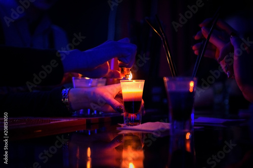 bartender makes burning alcoholic cocktail in shot glass on a table at night club