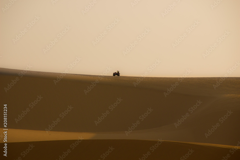 Quad bike riding on sand dunes at sunrise