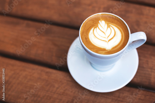 A cup of coffe with latte art on wooden table. Shot at angle with selective focus, italian cappuccino.