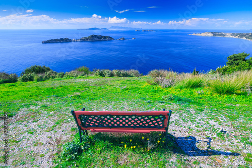 Obraz na płótnie Awesome view from red wooden bench to the coastline sea bay with crystal clear azure water, distant islands in the calm warm sea. Beautiful summer seascape. Agios Stefanos cape. Afionas. Corfu. Greece w salonie