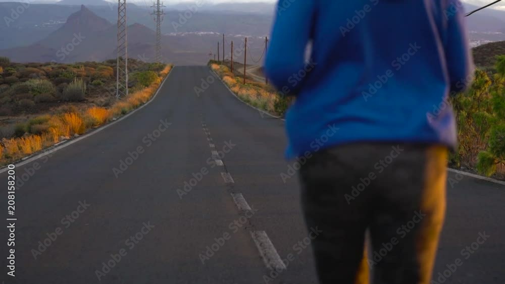 Woman runs along the deserted asphalt road at sunset, back view. Mountains on the background. Slow motion Woman runs along the deserted asphalt road at sunset, back view. Mountains on the background. Slow motion