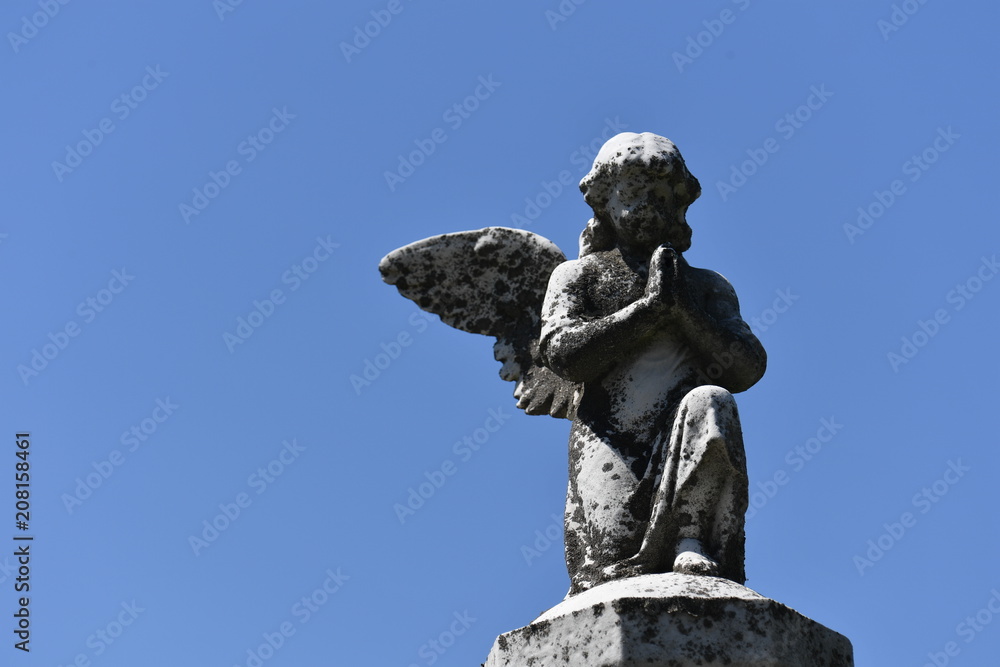 A weathered sculpture of a praying angel on a tomb of the cemetery of Quebec-Canada. A warm and sunny spring day A weathered sculpture of a praying angel on a tomb of the cemetery of Quebec-Canada. A warm and sunny spring day