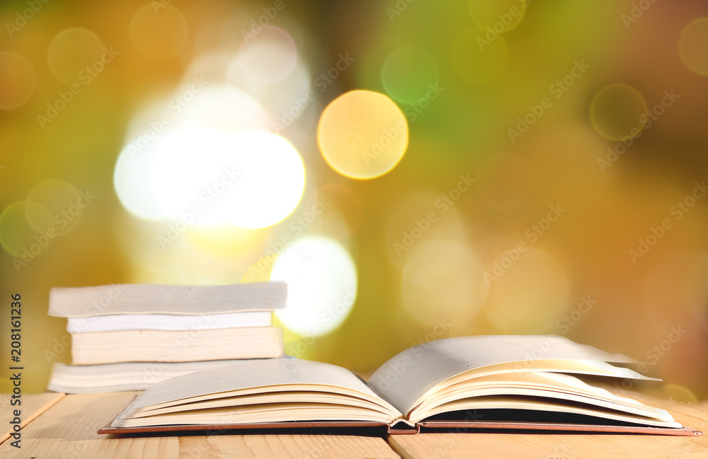 Opened book and pile of book on wooden table against bokeh light abstract background. Opened book and pile of book on wooden table against bokeh light abstract background.