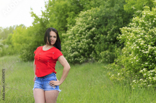 Beautiful young brunette in red t-shirt and short denim shorts at picnic photo