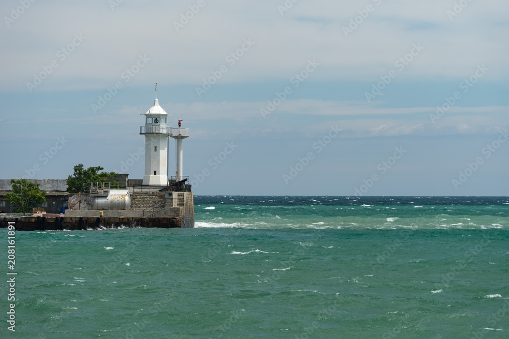 seascape with white lighthouse on the pier against the sea.