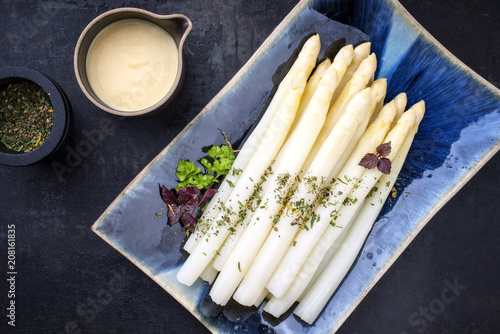 Traditional boiled white asparagus with sauce hollandaise and wine as top view on a blue plate