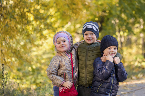 Group of happy three kids having fun outdoors in autumn park. Cute children enjoy hugging together against golden fall background. Best frend forever and happy childhood concept