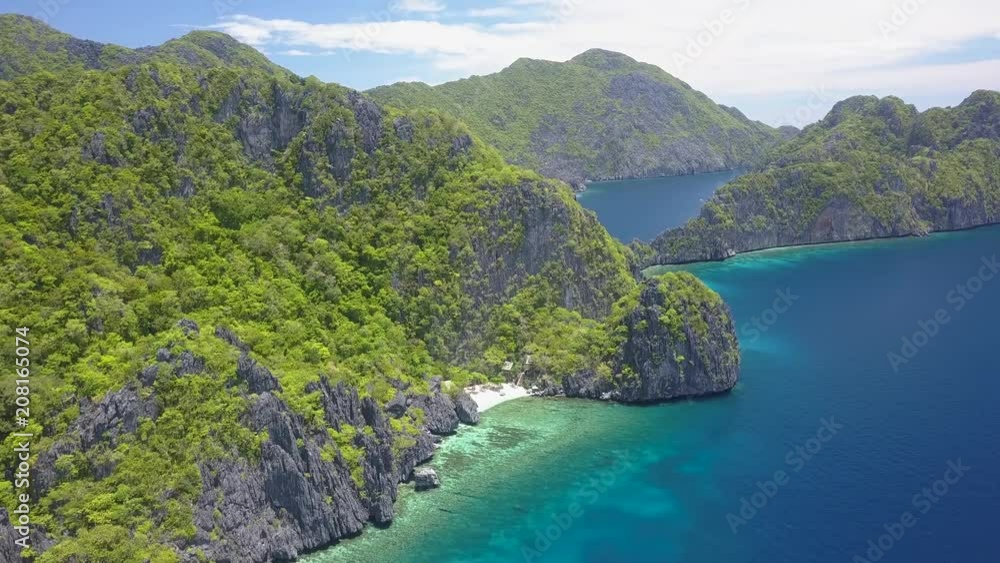 Aerial drone view flying along huge, tree covered limestone cliffs and a sandy beach surrounded by coral reef Aerial drone view flying along huge, tree covered limestone cliffs and a sandy beach surrounded by coral reef