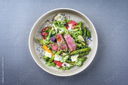 Modern spring salad with barbecue dry aged sliced fillet steak and green asparagus as top view on a plate with copy space