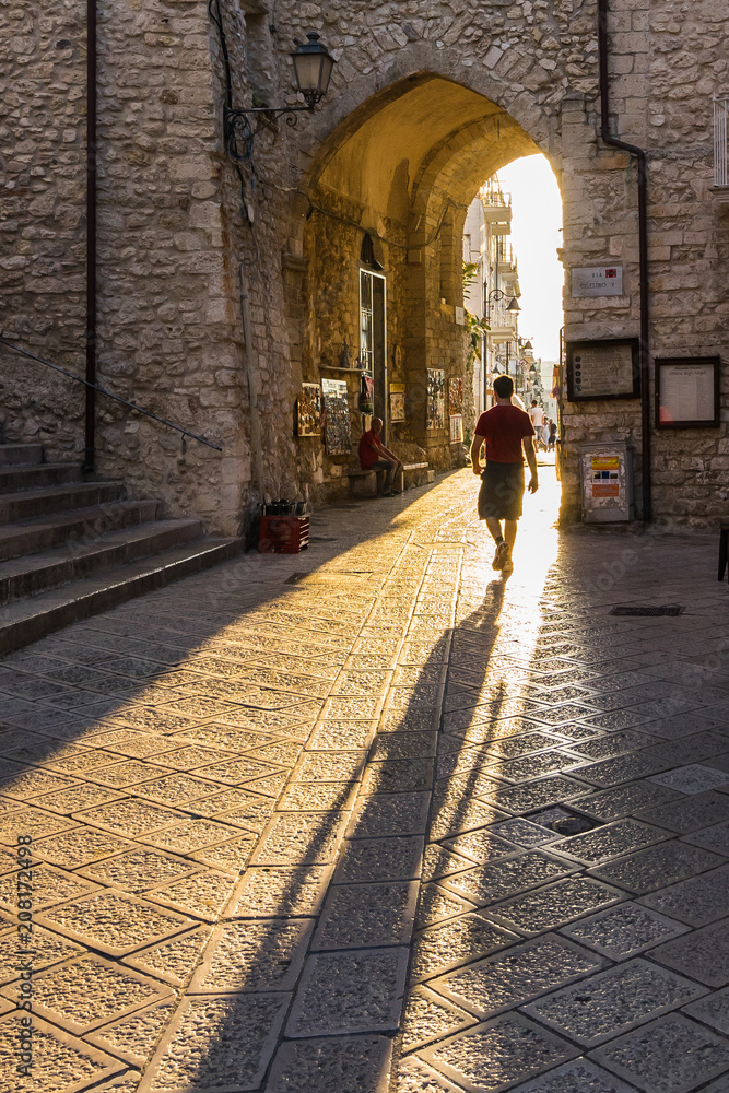Scenic view of historic centre of Vieste with an unidentified man with long shadow, Apulia, Italy