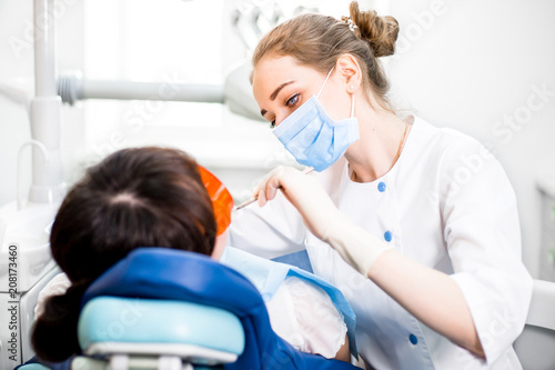 Girl dentist in a mask treats teeth to a patient in the clinic