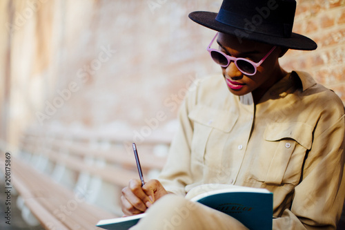 Portrait of a writer sitting on bench with sunglasses, writing by hand 