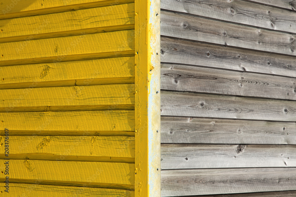 A corner of a wooden cabin with one wall painted in yellow and the other unpainted A corner of a wooden cabin with one wall painted in yellow and the other unpainted