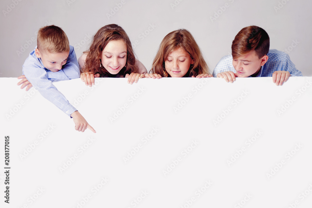 Children looking down behind white empty banner. Little kid behind pointing to white wall. Children looking down behind white empty banner. Little kid behind pointing to white wall.