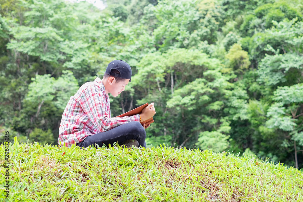 Young man sitting on green field and reads book.