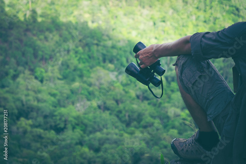 Young man hand is holding a binoculars with backpack relaxing on top of a mountain - scenery from vacation - photo with space for your montage.