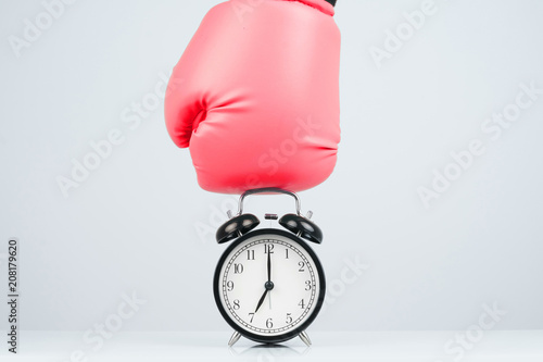 Red boxing gloves punching a classic alarm clock showing time.