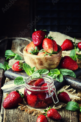 Strawberry confiture with whole berries, vintage wooden background, selective focus