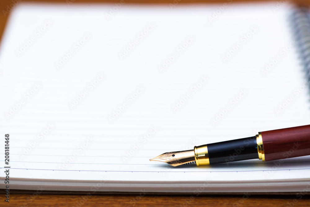 Close up of fountain pen or ink pen with notebook paper on wooden working table with copy space, office desk concept. shallow focus.