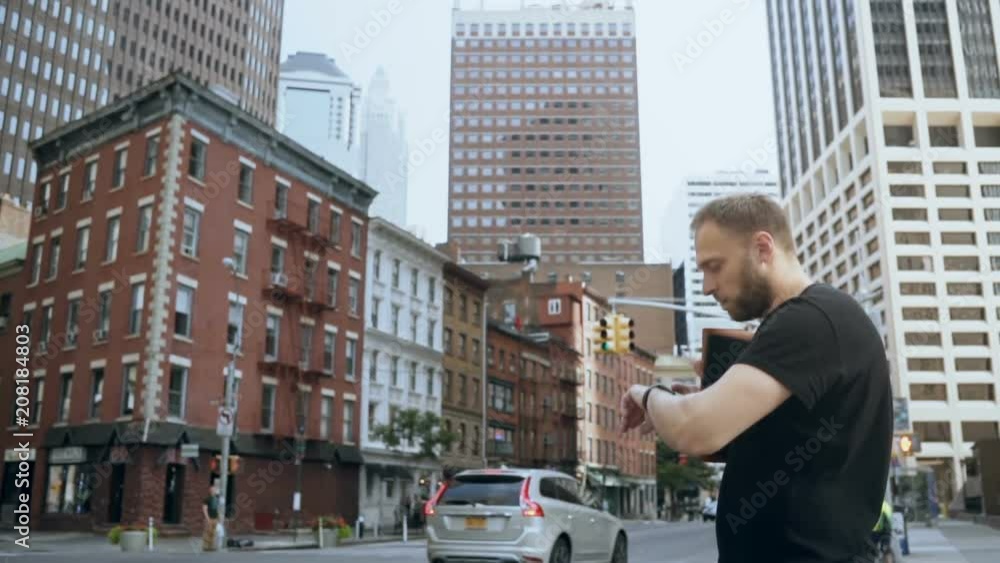 Young handsome man standing near the road and using the smart watch in financial district in New York. Slow motion. Young handsome man standing near the road and using the smart watch in financial district in New York. Slow motion.