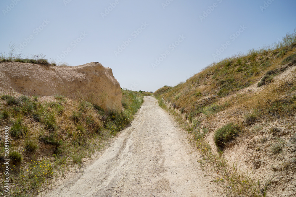 Walking unpaved rough sand trail route through landscape of dried ancient red valley with clear sky background, Cappadocia
