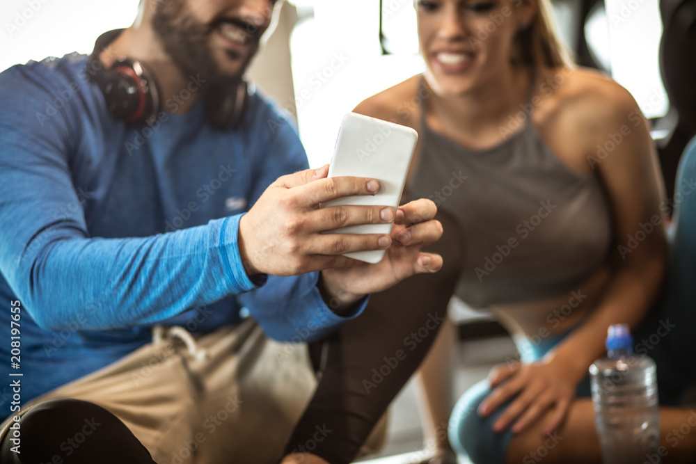 Personal trainer with  girl sitting on floor and having conversation after exercise. Using cell phone. Close up. focus is on hands.