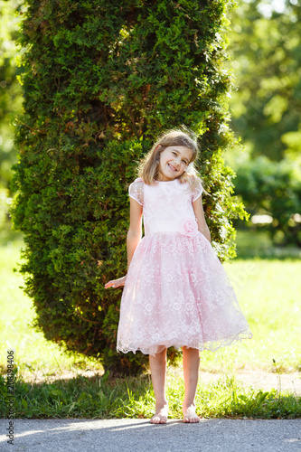 Portrait of a cheerful girl in a lush pink dress in the park.