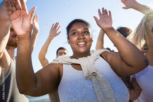Cheerful African-American woman smiling and dancing among friends while having fun during multiracial beach party.