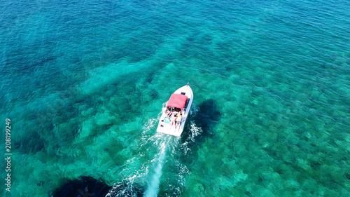Aerial drone bird's eye view photo of small boat cruising in tropical emerald clear waters