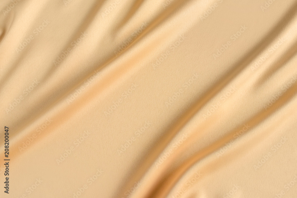 Close up of ripples in gold colored silk fabric. Satin textile background. Free copy space.