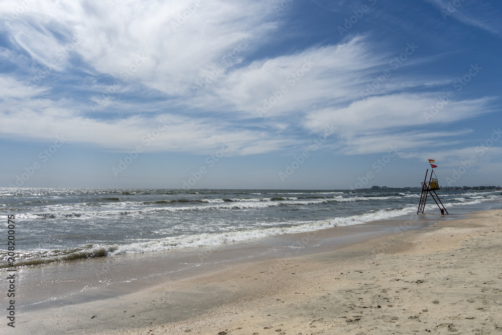 Empty lifeguard post at seaside, Mamaia beach, Romania; spring sunny day, clouds and waves