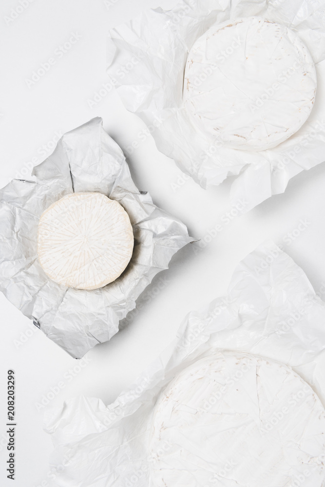 top view of organic brie cheese heads on crumpled paper and on white surface