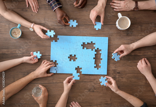 People with puzzle on wooden background, closeup of hands. Unity concept