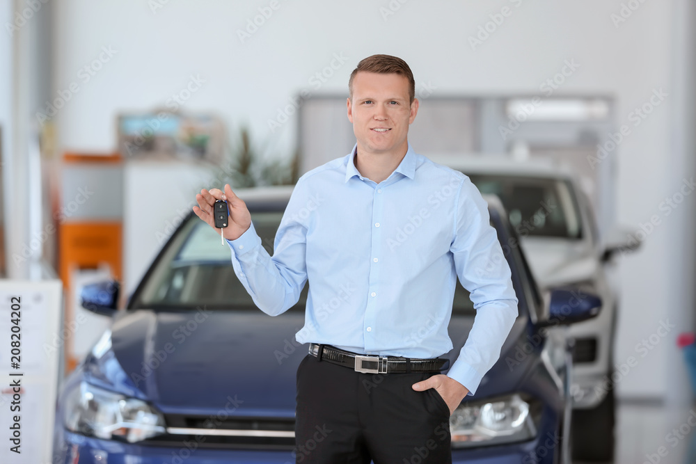 Handsome young salesman holding key in car dealership