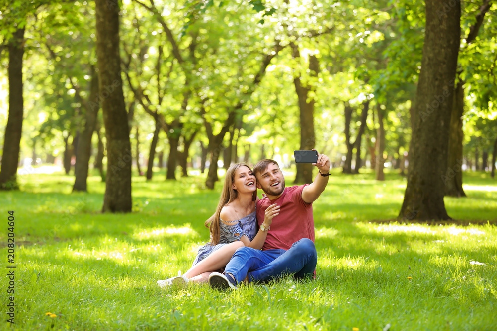 Happy young couple taking selfie on green grass in park