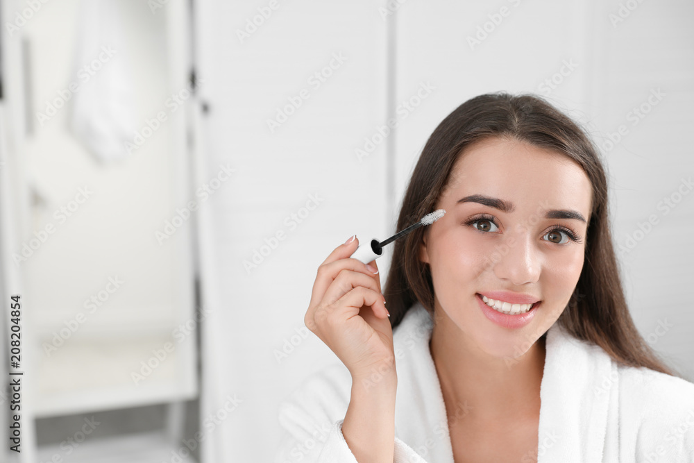 Attractive young woman applying oil onto her eyelashes indoors Attractive young woman applying oil onto her eyelashes indoors