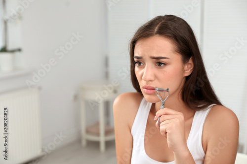 Young woman with eyelash loss problem holding curler indoors