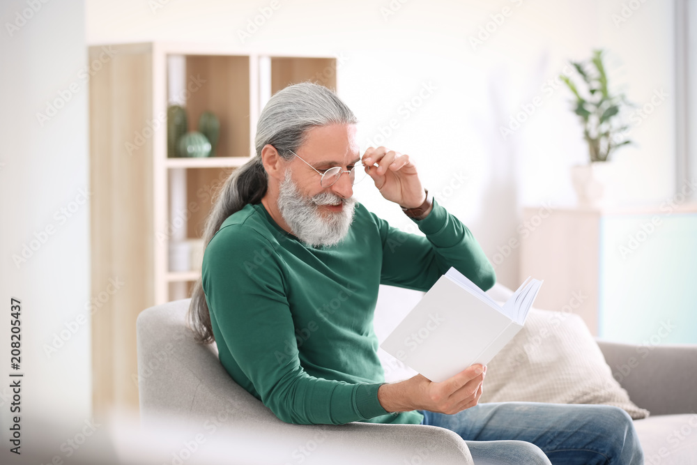 Handsome mature man reading book on sofa, indoors