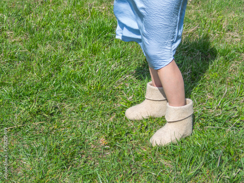 Cold summer. Women's feet in felt boots on the green grass background
