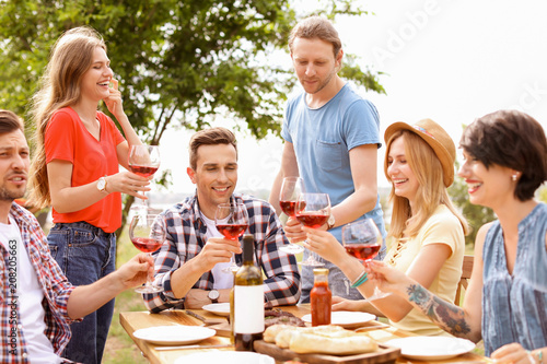 Young people with glasses of wine at table outdoors. Summer barbecue