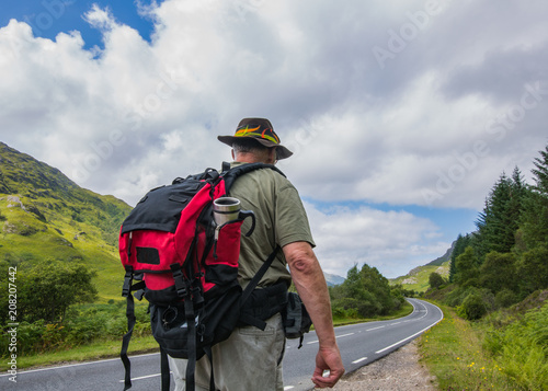 Mature active hiker with backpack walking away on the road. Europe travel