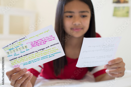 Girl Lying On Bed Using Written Study Cards To Help With Revision