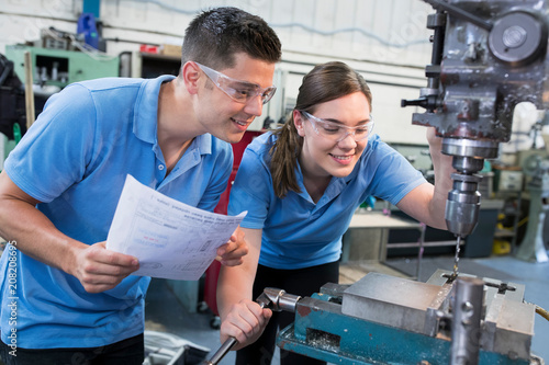 Engineer Instructing Female Apprentice On Use Of Drill